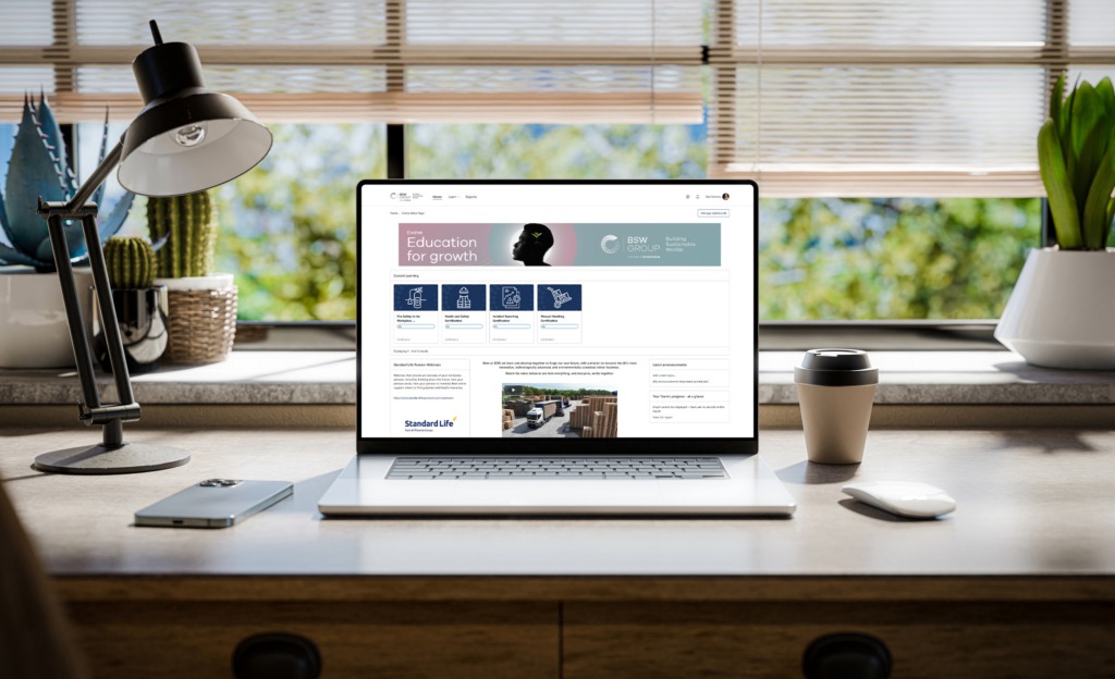 Ein Laptop mit einem Totara LMS-Bildschirm von BSW steht auf einem stilvollen Holzschreibtisch in einem Loft, mit Grünflächen im Hintergrund, die durch das Fenster sichtbar sind - 3d render